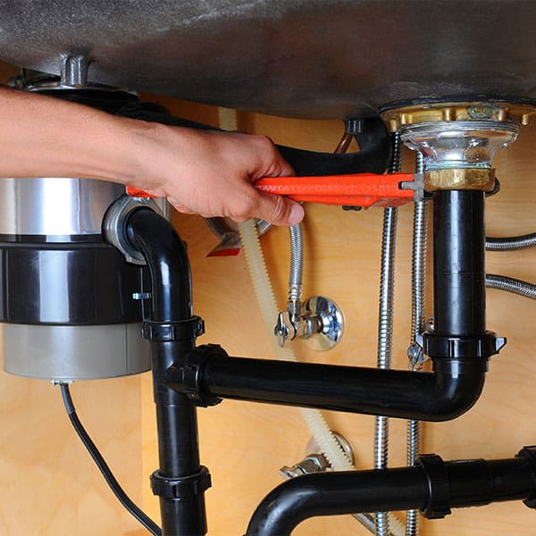 A plumber tightens a bolt unter a sink with an orange plumbers wrench